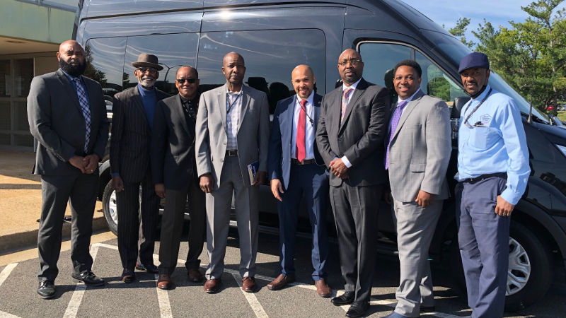 8 employees standing in front of a motorpool van